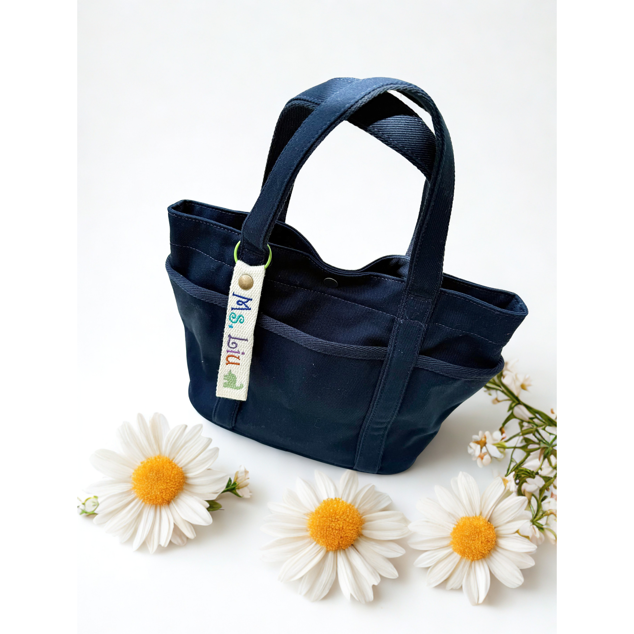 Flat lay of a handmade navy blue tote bag from Whimsy Handmade Studio, styled with embroidered name tag on a clean white background—evoking a fresh, natural vibe and highlighting artisanal craftsmanship.